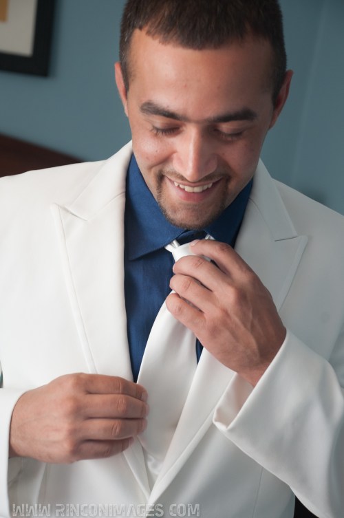 Groom wearing a white suit and navy blue shirt fixing his white tie before the wedding. -Wedding photographer puerto rico