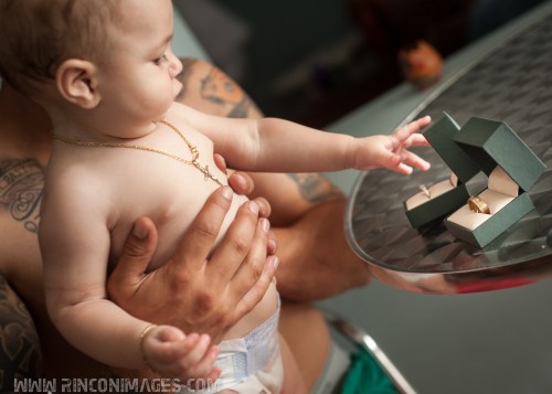 Their baby son wears a gold cross and plays with the wedding rings during a tender moment before the ceremony. Wedding photographer puerto rico