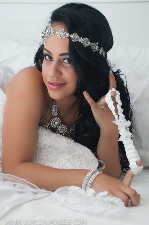 Bride suggestively plays with the garter belt while lying on her bed covered in her white wedding dress.