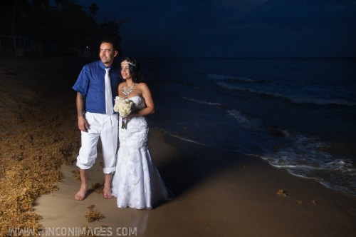 Bride and groom are barefoot on the beach. She is wearing a white wedding dress and holding a bouquet of white flowers. he is wearing a navy shirt with a white suit. wedding photographer puerto rico