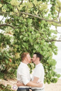 The happy couple kissing in front of the sea grape leaves, on the beach in Rincon Puerto Rico. LGBT wedding photographer Puerto Rico
